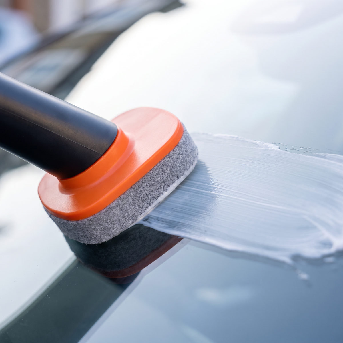 Close-up of the applicator spreading cleaning paste on windscreen glass